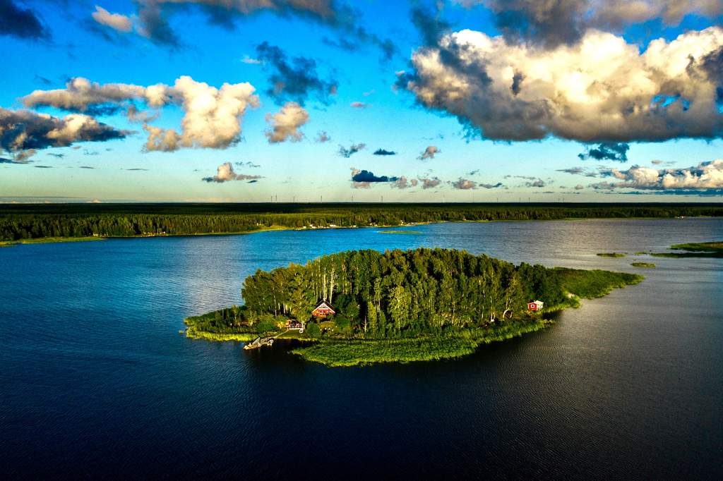 Majorsgrund ilmasta: metsäinen saari ja punaiset hirsitalot tyynessä, tummansinisessä meressä